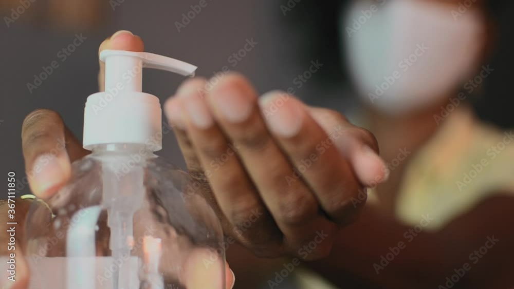 Close-up of the hands of a black woman applying gel sanitizer. Coronavirus prevention. New normal. Selective focus on the bottle on the foreground. Blurry background. Close-up of the hands of a black woman applying gel sanitizer. Coronavirus prevention. New normal. Selective focus on the bottle on the foreground. Blurry background.