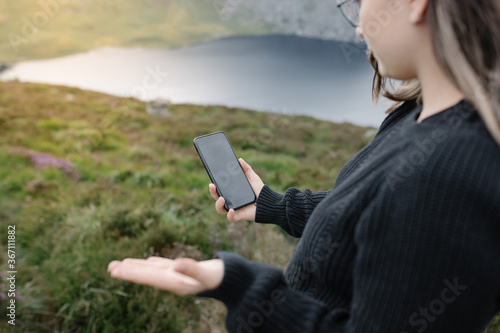 Young woman using her smartphone in the mountain with a beautiful lake, mountains and sunset in the background. Lifestyle concept