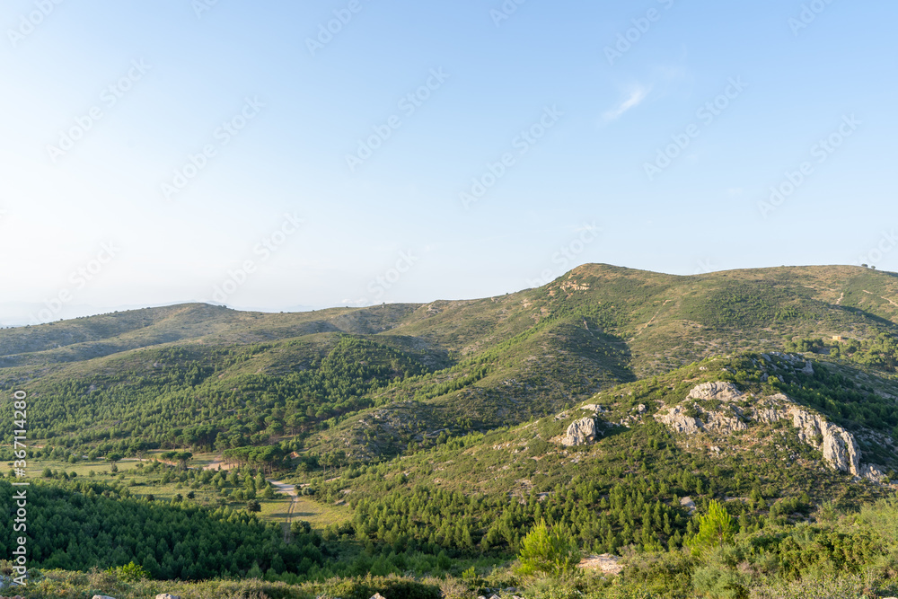 A landscape of mountains surrounded by hills and a path on a sunny day
