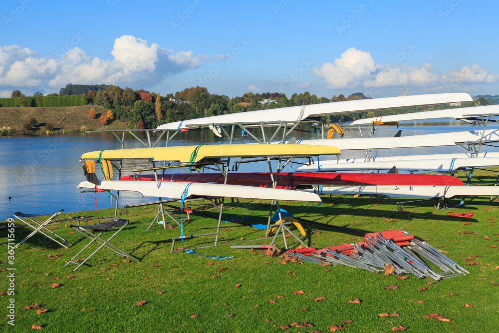 Racing boats on the grassy shore of a lake. Photographed at Lake Karapiro, New Zealand, one of the country's premiere rowing venues
