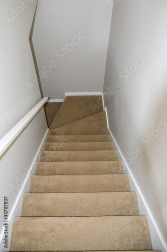 Top view of wooden stair covered by brown carpet in a modern white house with white wall