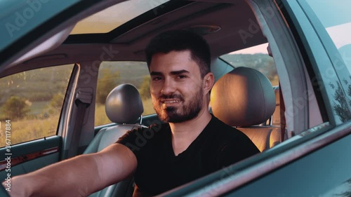 A handsome brunette man behind the wheel of a luxury car. The young man is excited and I hope he finally looks straight into the room and smiles resentfully at him photo