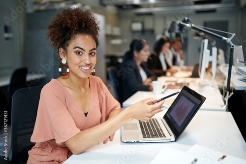 Portrait of smiling beautiful female design professional sitting with pen and laptop at desk in office