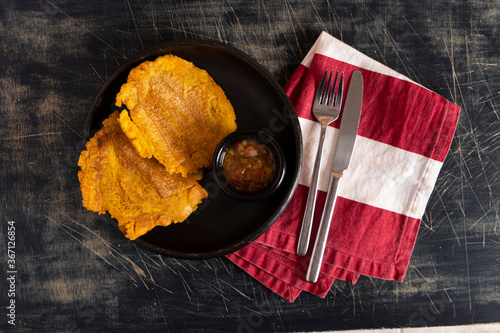 Plato de patacones colombiano con salsa de tomates y cebolla hogao. Persona comando plato tradicional latino. Platano pisado aplastado. photo