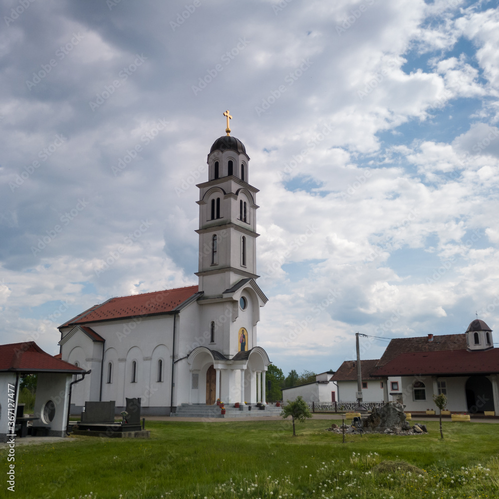 The village church in Bosanski Lužani dedicated to All Saints against the cloudy sky during the day. A temple building of simple architecture.