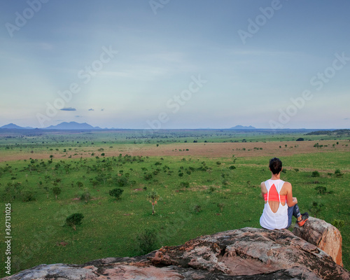 Young woman looking into the horizon of the beautiful landscapes of Kidepo Valley National Park, Uganda, Africa. The woman rests on top of a kopje after a nice hike.