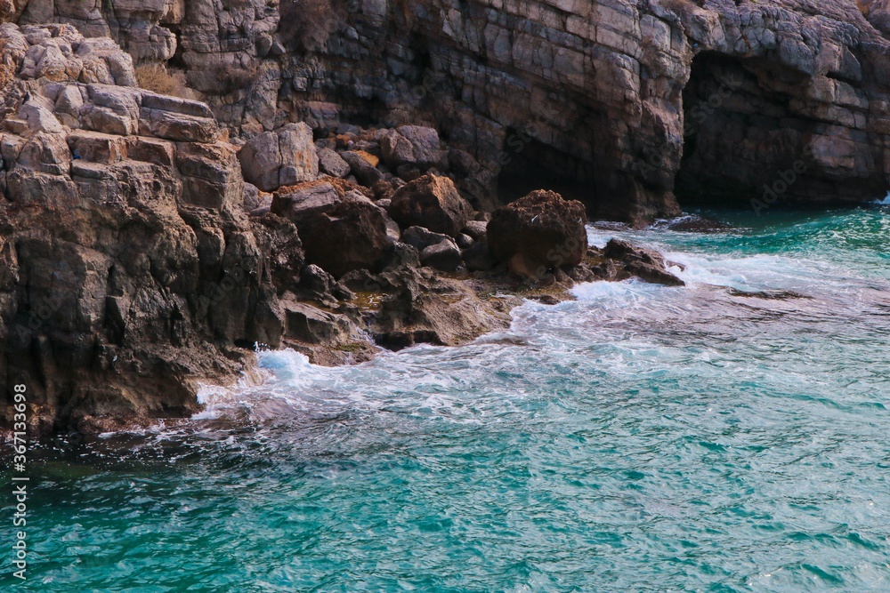 Naklejka premium blue sea hitting the rocky coast, cave in the sea