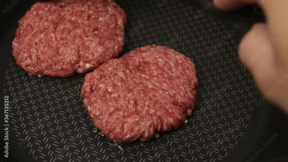 The chef puts beef patties into a frying pan. Juicy beef cutlet is fried in a pan. Close-up cooking beef cutlet for a burger. The chef puts beef patties into a frying pan. Juicy beef cutlet is fried in a pan. Close-up cooking beef cutlet for a burger.