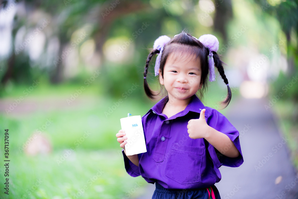 Asian girl drink milk. Child holds white milk box, a blue tube in her hand. Cute children to raise the thumb for admire or support drinking milk. Kid wore purple sportswear, black warm pants. 3 Years. Asian girl drink milk. Child holds white milk box, a blue tube in her hand. Cute children to raise the thumb for admire or support drinking milk. Kid wore purple sportswear, black warm pants. 3 Years.