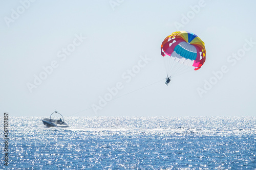 Parasailing in the sea. Small motor boat pulling a multicolored parachute with a couple of people. Selective focus. Horizontal orientation. photo