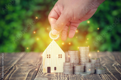 Businessman holding coin money on house wood model with coin many money stacks put on old wooden.