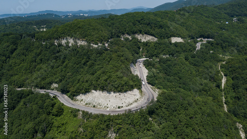 Aerial view from drone of curve road with a car on the mountain with green forest in Russia