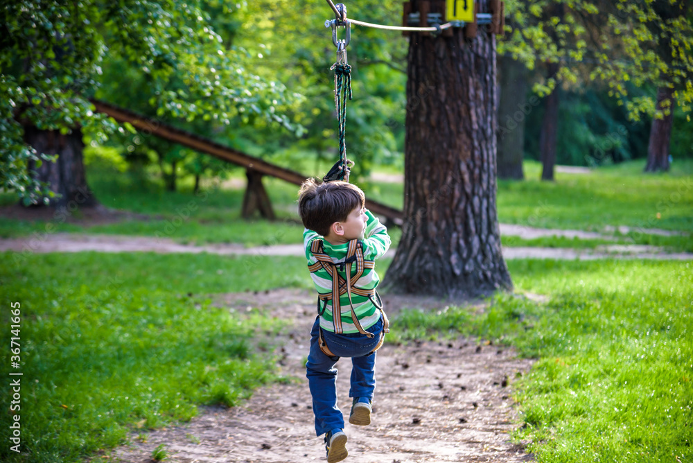 smiling boy rides a zip line. happy child on the zip line. The kid passes the rope obstacle course smiling boy rides a zip line. happy child on the zip line. The kid passes the rope obstacle course