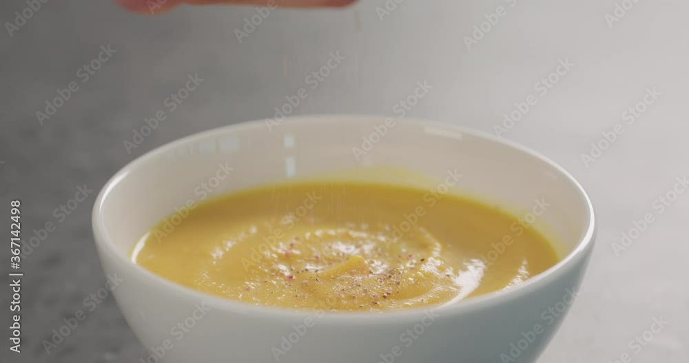 Slow motion seasoning pumpkin cream soup in white bowl closeup Slow motion seasoning pumpkin cream soup in white bowl closeup