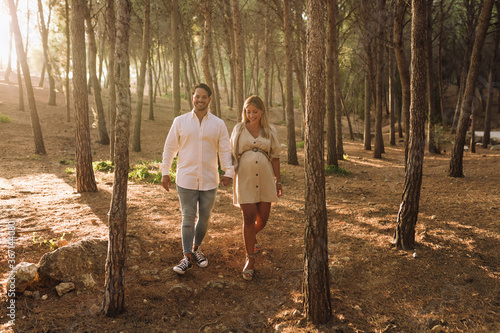 Pregnant couple walking in the woods. Pregnant blonde woman with her brunette boyfriend. 