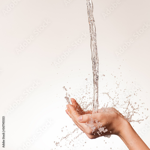 Photo of women's hands on which a stream of clean water pours. Human hands with falling water and spray isolated on white. Cleanliness and hygiene of the body. Girl's hand with water drops.