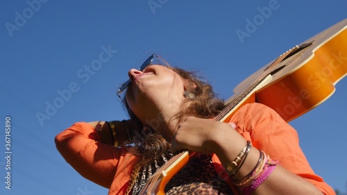 nature, summer vacation, vacation and people concept - happy smiling woman in sunglasses stands with a guitar on her shoulder photo