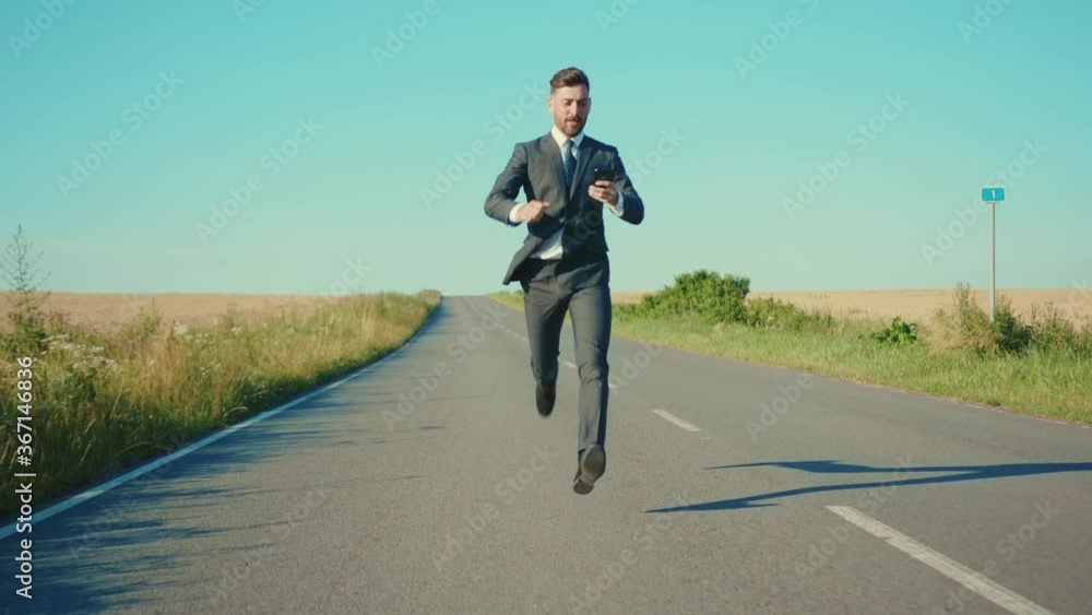 Slow motion businessman runs talking on a smartphone country road near a wheat field freedom concept outdoors handsome winner elegant close up Slow motion businessman runs talking on a smartphone country road near a wheat field freedom concept outdoors handsome winner elegant close up