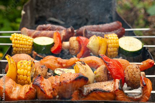 Variety of meat, fish and vegetable ingredients put on metal skewers and placed over charcoal grill.