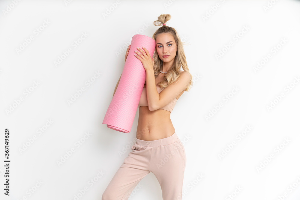 Fototapeta premium Skinny sporty blonde Girl in sportwear posing with pink mat
