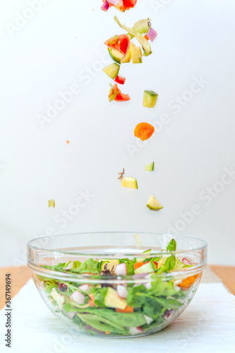 Pieces of fresh vegetables falling down into glass bowl creating healthy salad.