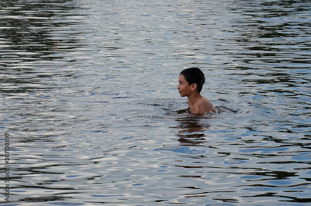 A happy boy is swimming in the lake. A happy child stands in the sea. Laughing young boy in the water. Recreation, summer, healthy lifestyle.