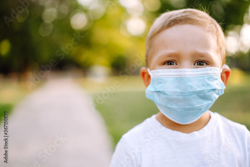 Portrait of little boy with medical face mask in the park during pandemic. Concept of health and safety life from coronavirus. Covid-2019. Kids safety.