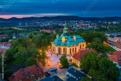 Aerial view of baroque church temple in the heart of Karkonosze mountains in Jelenia Gora surrounded by old city architecture at beautiful sunset. Photo taken from drone. Popular tourist destination photo