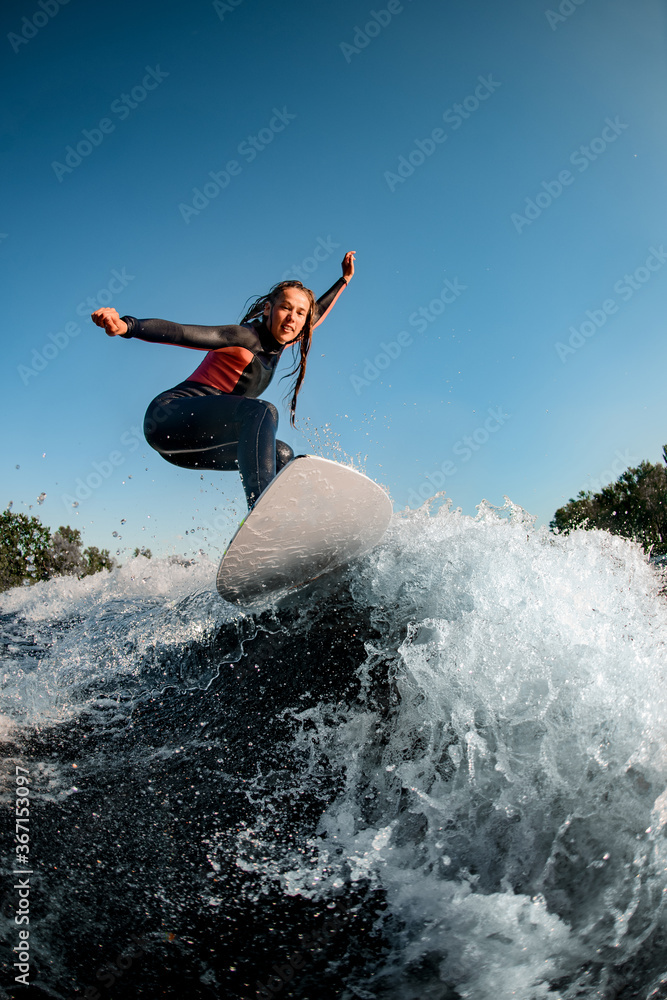Active young wet woman in wetsuit stands on surfboard and rides on the wave. Active young wet woman in wetsuit stands on surfboard and rides on the wave.