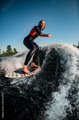 Wet woman athlete rides down the wave on surfboard against clear blue sky