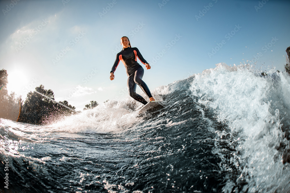 View on wet woman athlete who rides down the wave on surfboard against clear blue sky