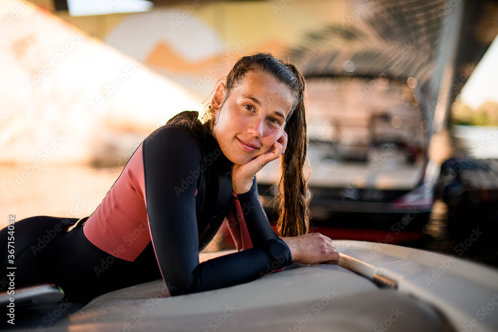 portrait of young woman wearing a black wetsuit lies with her head propped with her hand