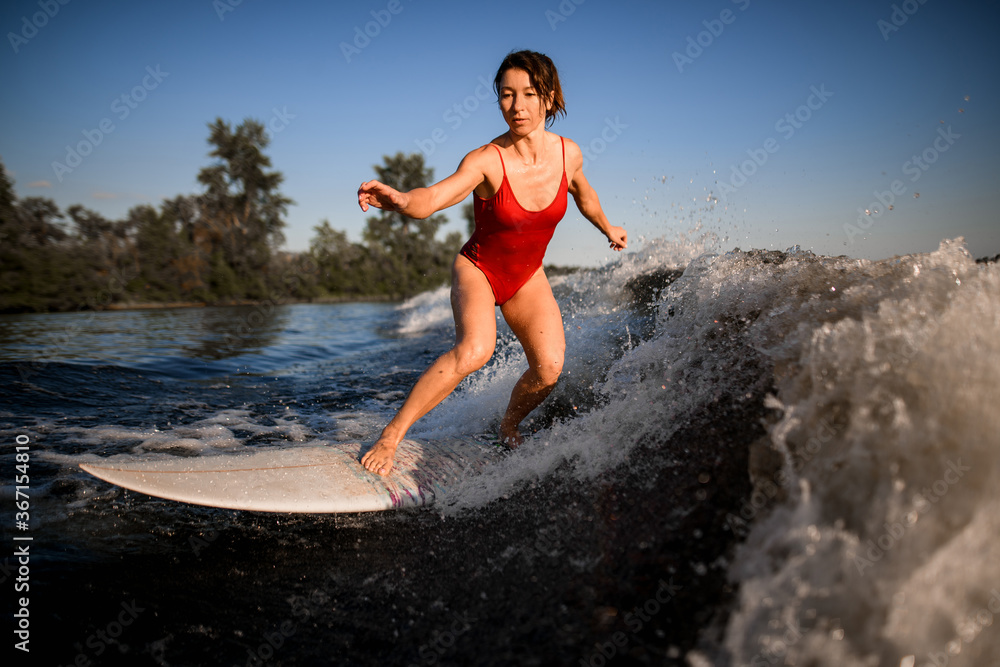 Side view of active woman who rides the wave on surfboard