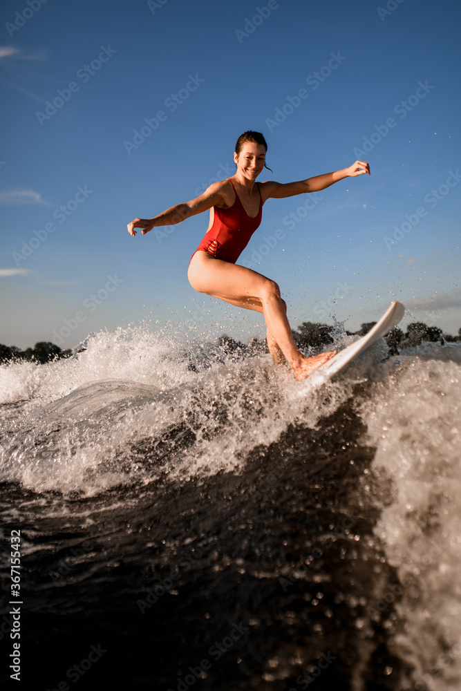 Smiling female wakesurfer in red swimsuit rides up the wave on surfboard Smiling female wakesurfer in red swimsuit rides up the wave on surfboard