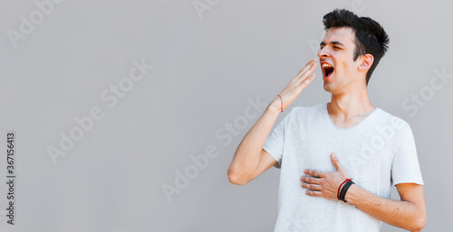 Exhausted young man yawning isolated on grey background photo