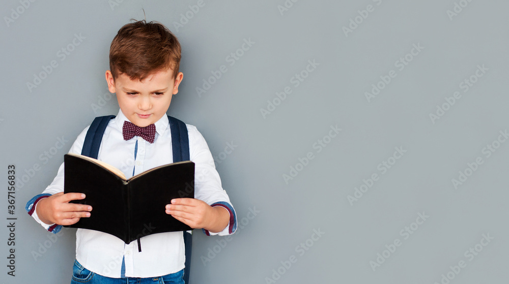Obraz premium Cute little boy reading book on grey background