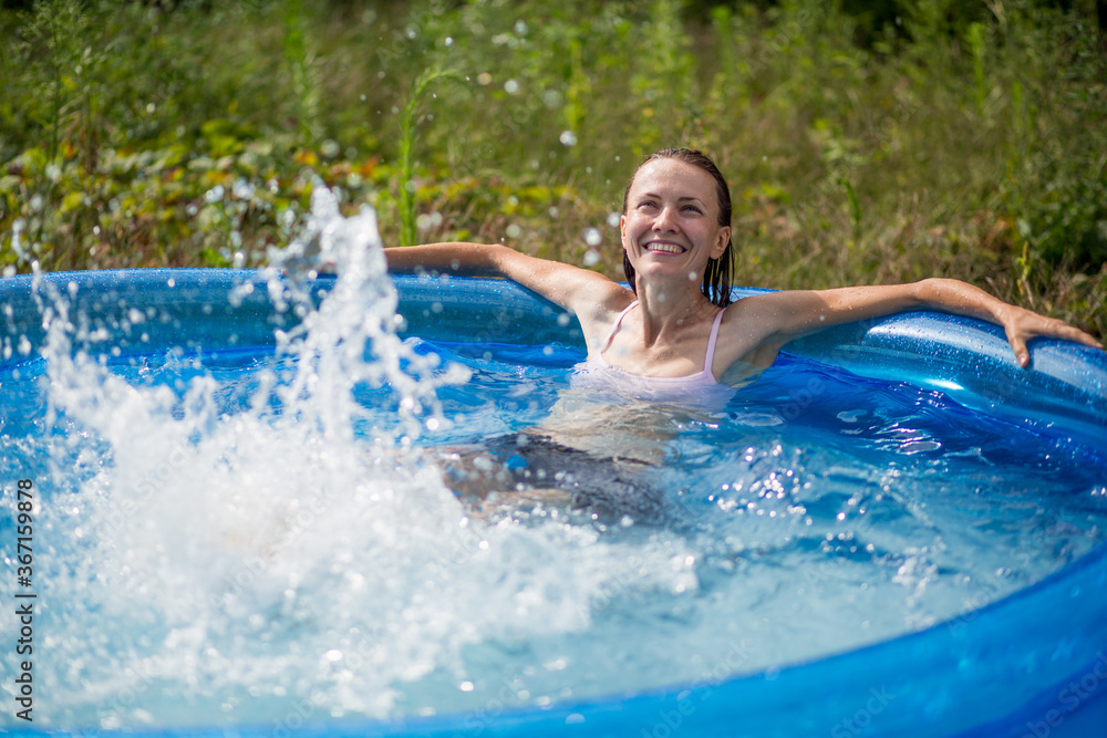 Beautiful woman splashing in inflatable swimming pool outdoor, having fun