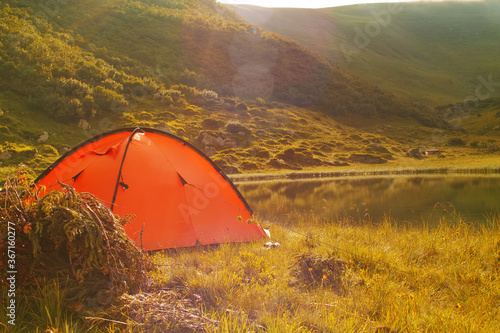 Orange tent near the lake in the mountains