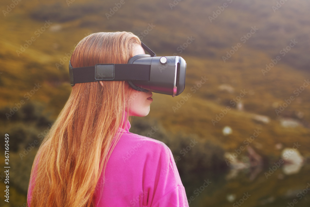 Woman in virtual reality glasses standing near a mountain lake