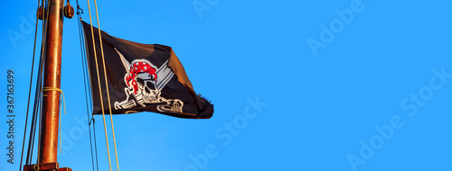 The pirate flag or the Jolly Roger - old shabby black flag with a skull waving on the mast of a sailing ship
