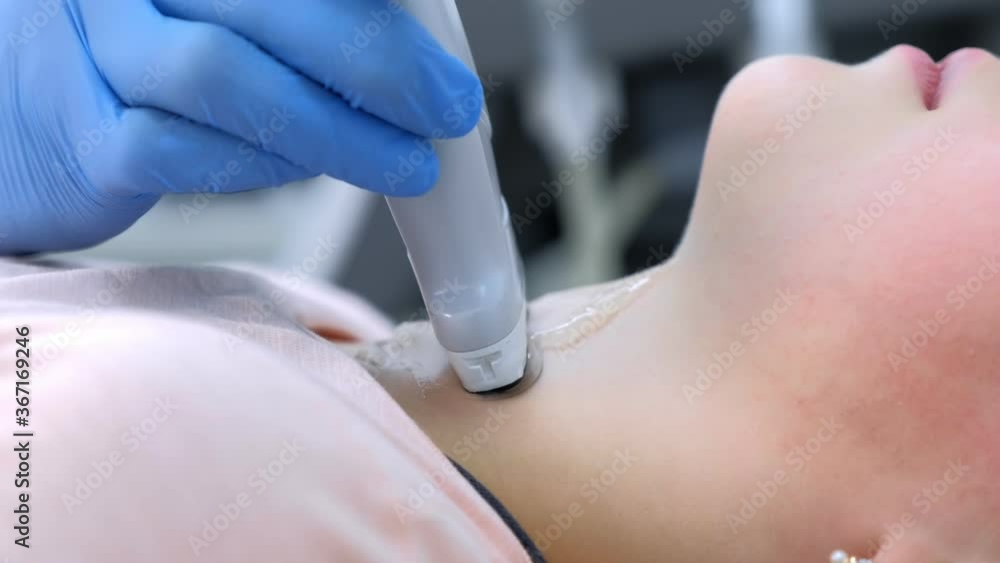Doctor diagnostic examining patient child girl thyroid gland using ultrasound scanner machine, hands closeup. Girl lying on couch, side view. Run ultrasound sensor over patient neck looking at screen. Doctor diagnostic examining patient child girl thyroid gland using ultrasound scanner machine, hands closeup. Girl lying on couch, side view. Run ultrasound sensor over patient neck looking at screen.