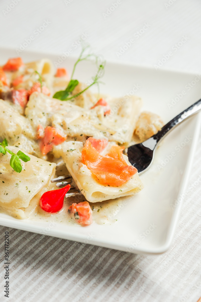 A close-up of paccheri pasta with cream sauce and salmon on a fork, on a white plate A close-up of paccheri pasta with cream sauce and salmon on a fork, on a white plate