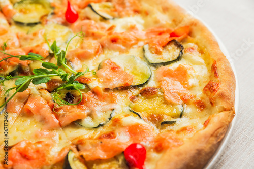 A close-up of a pizza with zucchini, red fish and cheese, on a white plate