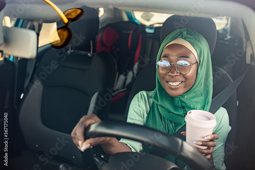 Middle Eastern Woman Driving a Car, and drinking coffee to go. Arab women driving car. Muslim Woman wearing light hijab in a car lifestyle shoot. photo