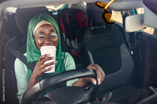  Beautiful muslim woman with toothy smile driving car. Portrait of a Middle Eastern woman driving a car, she is wearing a modern green Abaya. She is drinking coffee to go. photo
