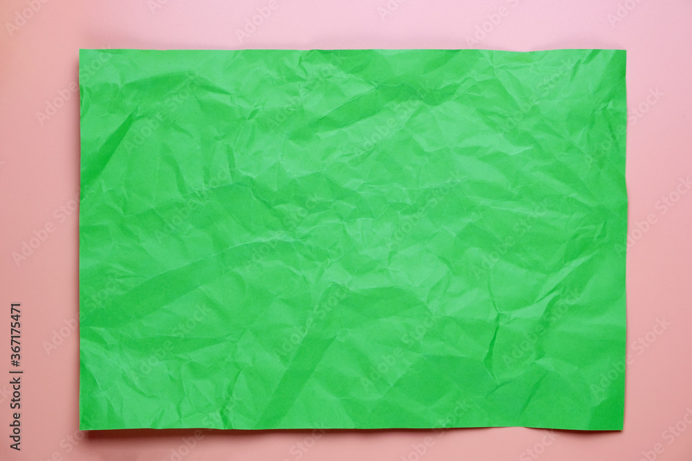 Close up of green crumpled empty sheet of paper on pink background.