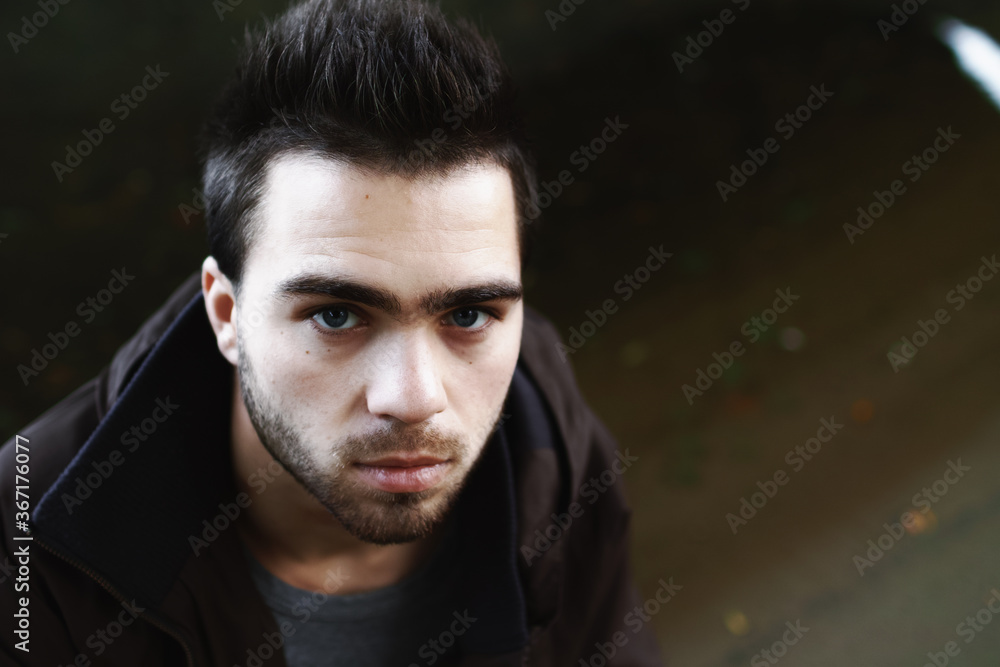 Fototapeta premium Close-up of a young brunette male alcoholic on the street under the bridge.