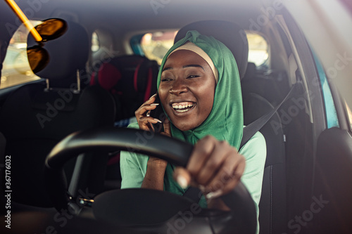 Muslim businesswoman on a business trip, driving a car and talking with smartphone. miling black muslim woman driving her vehicle. Happy muslim woman driving car © Dragana Gordic