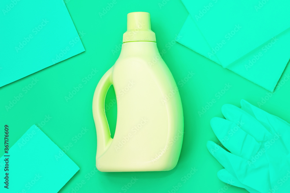Yellow bottle in the centre, green rags, green gloves on a green background. Cleaning concept Yellow bottle in the centre, green rags, green gloves on a green background. Cleaning concept