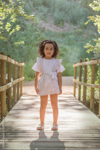 Girl in striped tank top on a wooden bridge in a grove.